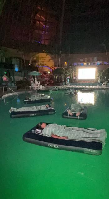 Guests floating on rafts in the green-lit pool during a sound bath